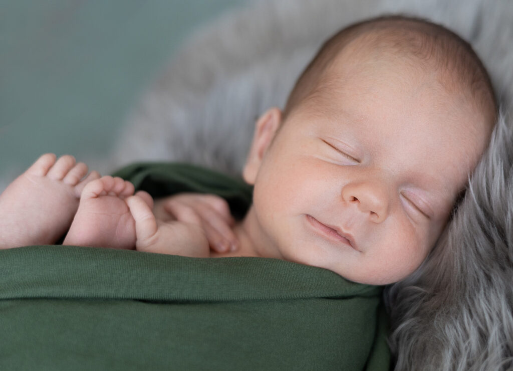 Neugeborenes Baby im grünen Tuch, schlafend beim Fotoshooting mit Newbornfotografin Anika Hellemann